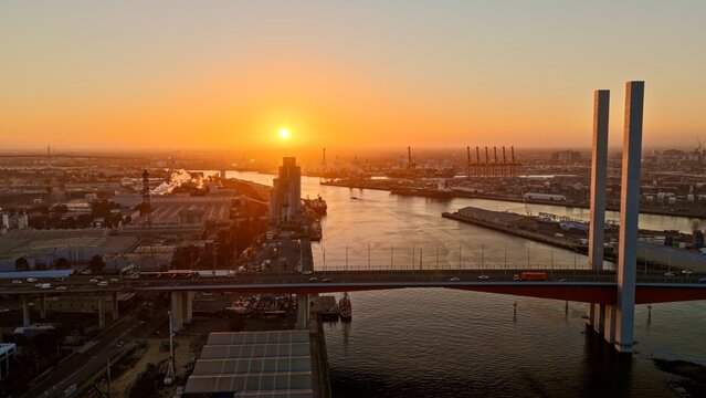 Port Melbourne, Victoria, Australia &ndash; 4K aerial drone view of Bolte Bridge over Yarra River, Port of Melbourne container terminal and industrial waterfront at golden sunset