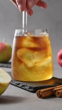 Hand slowly stirs apple cider cold brew tonic with glass straw, mixing coffee and cider over ice.