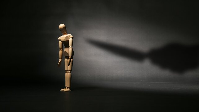 Sad wooden mannequin standing alone with a knife shadow pointing at its back, symbolizing betrayal, backstabbing, or hidden danger.