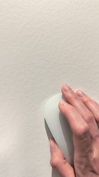 Hand using computer mouse on a clean white desk with ample negative copy space. Corporate employee navigates through an internet site or business database using wireless hardware. Top down
