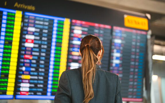 Standing passenger looking flight information status board at international airport terminal