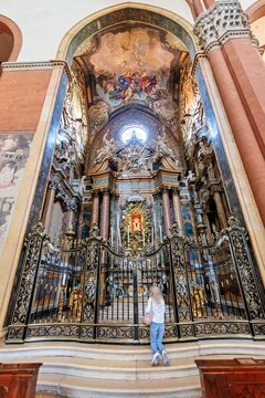 View of a woman kneeling before an ornate baroque altar with intricate gold carvings and marble columns inside Basilica of San Petronio in Bologna, Emilia-Romagna, Italy.