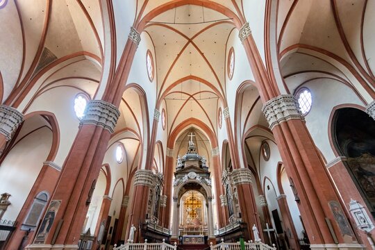 View of the interior of the Basilica of San Petronio featuring tall Gothic columns, ribbed vaulted ceilings, and ornate altar in Bologna, Emilia-Romagna, Italy.