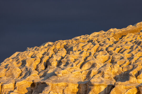 View of the textured limestone formations of Tuzbair illuminated by golden hour light against a dark, dramatic sky in Mangystau District, Mangystau Region, Kazakhstan.