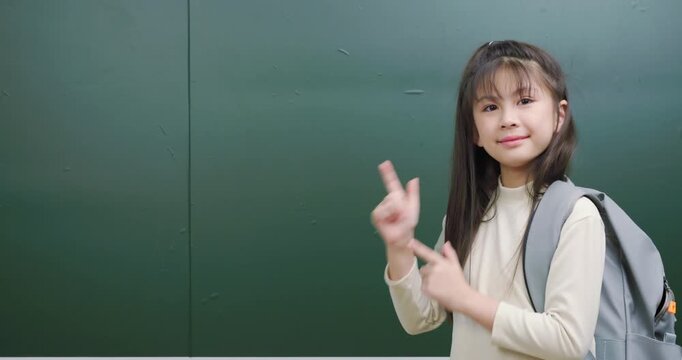 Cute Asian student pointing fingers to the side presenting copy space for text.