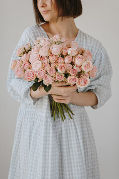 Young brunette woman wearing vintage blue gingham dress while posing with fresh pink roses
