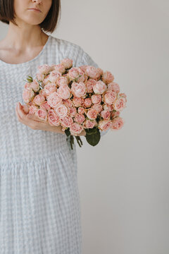 Studio portrait of graceful woman in checkered blue dress holding romantic pink rose bouquet