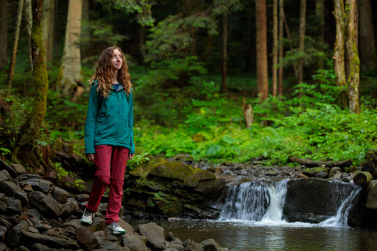 Woman hiking through a lush forest with a small waterfall and stream lifestyle portrait with cheesing smiling face
