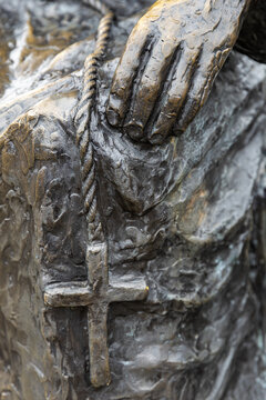 View of a detailed bronze sculpture of a hand resting on a cross, capturing the textured metal surface and religious symbolism in Monnickendam, North Holland, Netherlands.