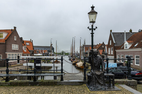 View of a bronze monk statue by a canal in Monnickendam, with traditional Dutch houses and moored sailing boats in the background, Monnickendam, North Holland, Netherlands.