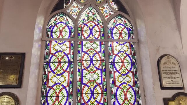 Colorful stained glass window inside historic church with Gothic arch design, intricate geometric patterns and bright decorative panels, showcasing Christian architecture, heritage and sacred interior