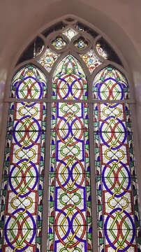 Colorful stained glass window inside historic church with Gothic arch design, intricate geometric patterns and bright decorative panels, showcasing Christian architecture, heritage and sacred interior