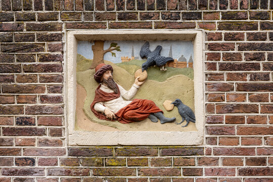 View of a stone relief sculpture on a brick wall depicting a bearded man in a turban holding a loaf of bread with two ravens in Monnickendam, North Holland, Netherlands.