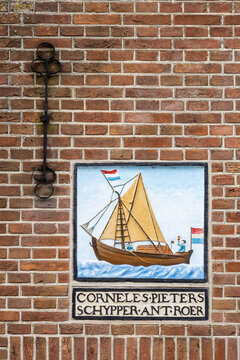 View of a traditional Dutch sailing ship plaque with the inscription Corneles Pieters Schypper Ant Roer mounted on a red brick wall in Monnickendam, North Holland, Netherlands.