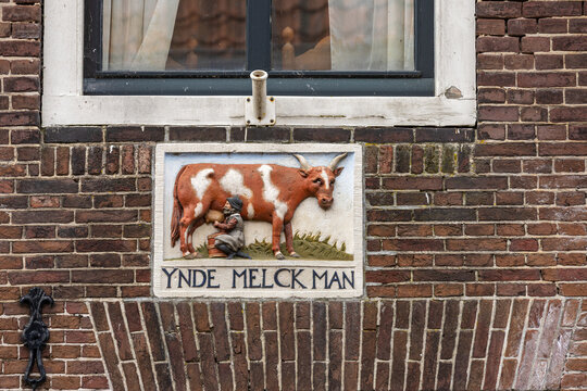 View of a historic facade stone depicting a man milking a cow with the inscription Ynde Melck Man on a traditional brick wall in Monnickendam, North Holland, Netherlands.