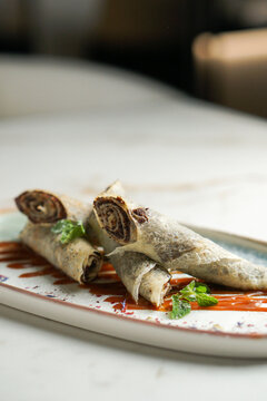 Rolled thin Russian blini filled with poppy seed paste, served on a plate with berry sauce and fresh mint traditional Maslenitsa dessert or breakfast. High quality photo