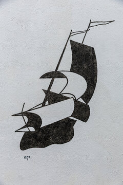 View of a minimalist black line drawing of a historic sailing ship with the year 1573 painted on a textured white wall in Monnickendam, North Holland, Netherlands.