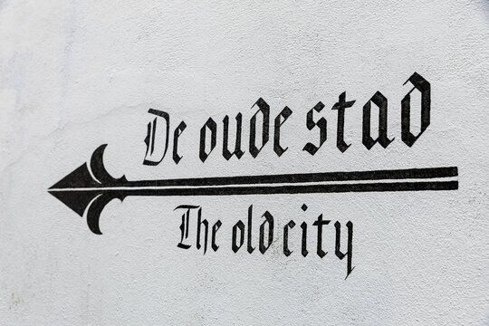 View of a painted sign on a white wall with an arrow pointing the way to the old city, featuring black gothic lettering in Monnickendam, North Holland, Netherlands.