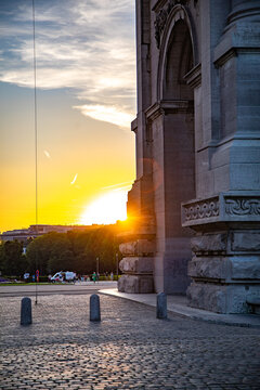View of the Cinquantenaire Arch at sunset with warm golden light illuminating the stone structure and cobblestone ground in Brussels, Brussels, Belgium.