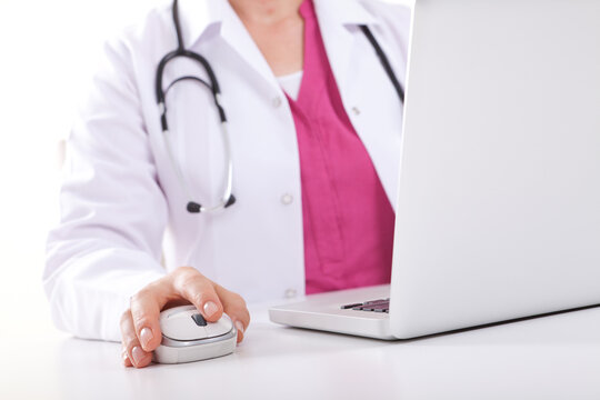 Close up of female doctor or nurse in lab coat using computer mouse next to laptop isolated on white background.