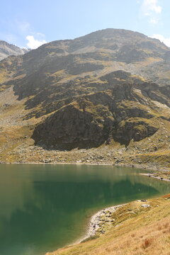 View of the alpine lake in Madesimo surrounded by rocky mountain slopes and grassy terrain under a clear blue sky in Madesimo, Lombardy, Italy.