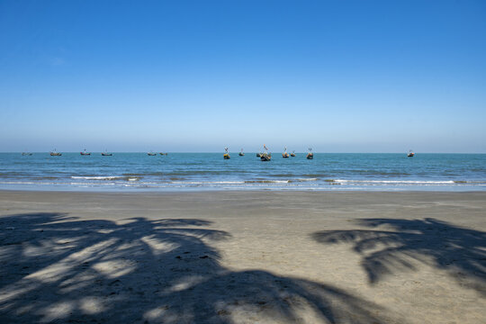 View of fishing boats on the calm blue sea off Saint Martins Island with palm tree shadows on the sandy beach in Cox's Bazar District, Chittagong Division, Bangladesh.