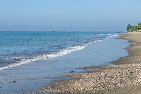 View of Saint Martins Island beach with fishing boats on the horizon and gentle waves washing onto the sandy shore in Cox's Bazar District, Chittagong Division, Bangladesh.