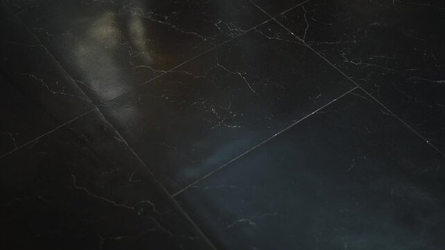 A cleaning machine moves across a black floor, removing dirt and stains. The area appears shiny and clean after the scrubber has passed