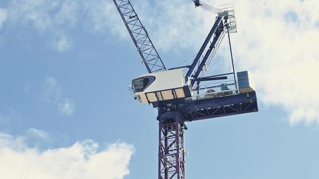 A construction crane lifts equipment high into the air, showing strong support for heavy loads. The crane is set against a bright blue sky with scattered clouds