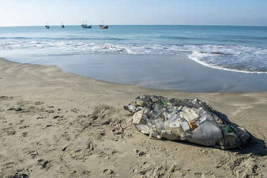 View of plastic waste collected in a net on the sandy shore of Saint Martin's Island West Beach with fishing boats on the horizon in Cox's Bazar District, Chittagong Division, Bangladesh.