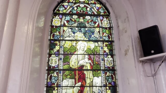 Historic stained glass church window depicting Jesus Christ as the Good Shepherd with sheep, colorful religious art, Gothic arch design, Christian heritage, sacred architecture and spiritual symbolism