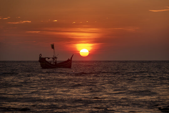 View of a traditional wooden fishing boat silhouetted against a vibrant sunset over the sea at Saint Martins Island, Cox's Bazar District, Chittagong Division, Bangladesh.