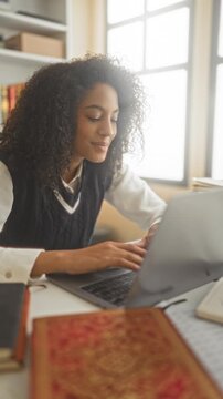 Young woman student typing on laptop with hands on keyboard at a desk in building, books and notebook nearby; concentration learning.