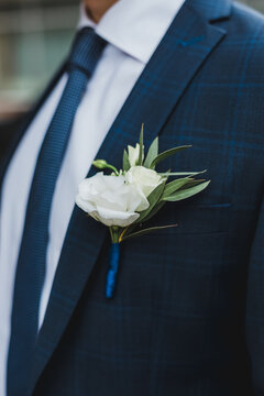 Elegant boutonniere with fresh white rose pinned to groom blue checkered suit jacket for wedding ceremony.