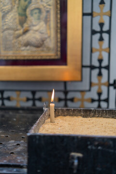 View of a single burning candle placed in a sand-filled metal container inside a church in Coptic Cairo, with a blurred religious icon in the background, Cairo, Cairo Governorate, Egypt.