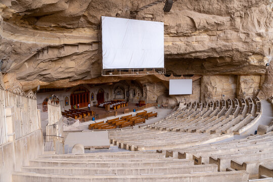 View of the Cave Church, a large amphitheater carved into the Mokattam mountain, featuring stone seating, a large projection screen, and an altar area in Cairo, Cairo Governorate, Egypt.
