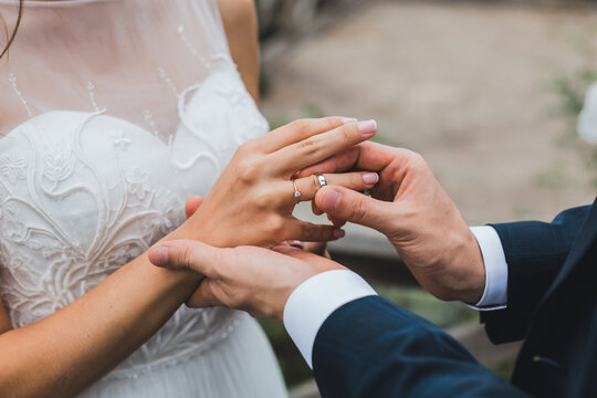 Romantic close-up of groom placing silver wedding band on bride finger outdoors.