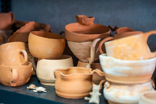 Collection of handmade ceramic cups and bowls displayed in pottery workshop. Unfinished pottery represents craftsmanship and stages of artisan ceramic production