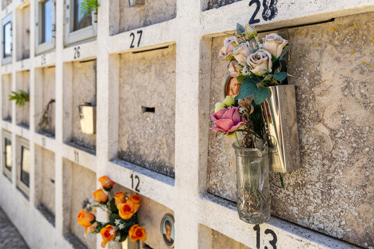 View of numbered burial niches in a cemetery wall adorned with artificial flowers in Santiago do Cacem, Setubal, Portugal.