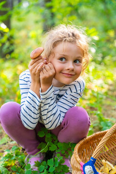 Happy young girl showing mushroom she found while foraging in forest. Childhood discovery represents curiosity, nature exploration and joy of mushroom picking