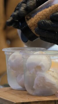 Vertical video. Street vendor pouring fresh coconut milk over a scoop of coconut ice cream and sprinkling crushed nuts as a finishing touch