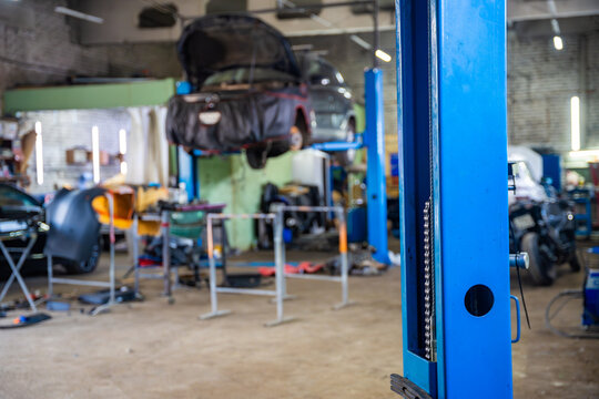 Car raised on vehicle lift with open hood inside auto repair shop. Workshop scene represents professional maintenance and used car service