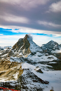 View of the snow-covered Matterhorn peak under a dramatic sky with clouds and blue patches in Zermatt, Valais, Switzerland.
