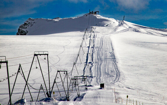 View of a T-bar ski lift on the snow-covered glacier with tracks on the slope and a clear blue sky in Zermatt, Valais, Switzerland.