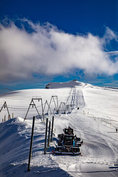View of a snow groomer preparing the ski slopes near the Matterhorn with ski lift infrastructure under a clear blue sky in Zermatt, Valais, Switzerland.