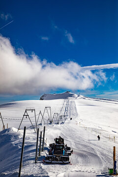 View of a snow groomer on a snowy mountain slope with ski lift infrastructure under a clear blue sky in Zermatt, Valais, Switzerland.