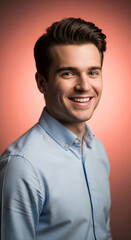 Obraz premium Close-up portrait of a smiling young man in a light blue shirt against a peach background, symbolizing confidence, professionalism, and positivity, ideal for business and lifestyle themes