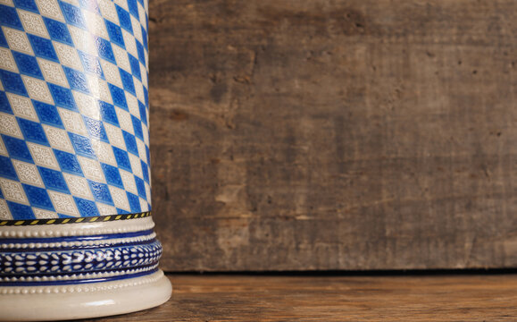 A Bavarian beer mug with a bavarian flag in front of a wooden background with space for text