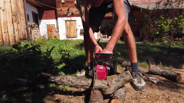  Man cutting through a wooden log with cordless chainsaw 