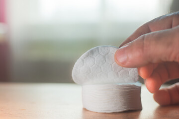 The image shows a hand holding a round cotton pad. The cotton pad is lying on a wooden surface. © Valeryi